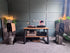 A styled home audio setup in a room with paneled gray walls and a gray carpet, featuring a wooden console table with audio equipment, two large speakers on stands, and vinyl records.